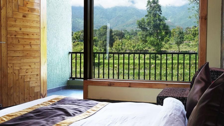 Bedroom with large glass window offering scenic mountain and forest views at Corbett Nirvana Resort.