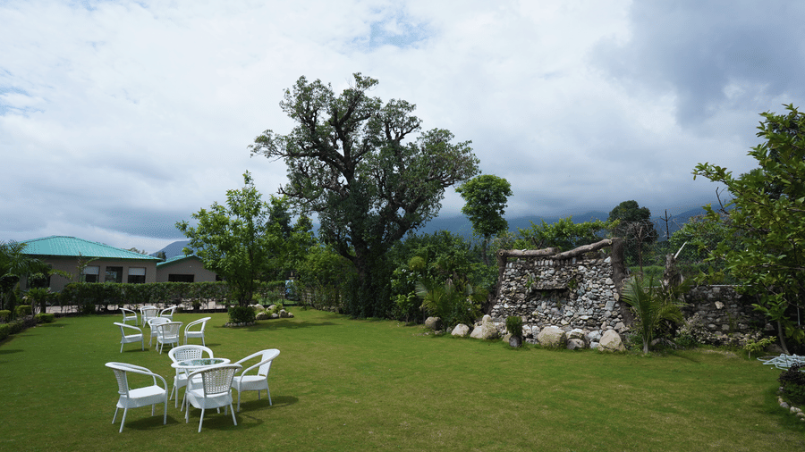 A wide-angle shot of an expansive lawn area with a stone wall in the middle of the fences at Corbett Nirvana Resort.