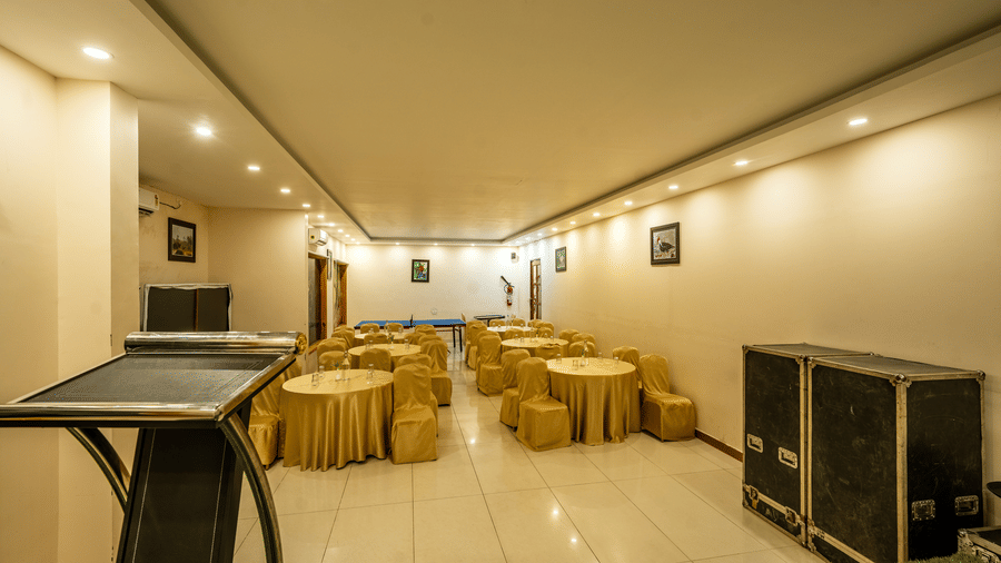 Banquet hall at Corbett Nirvana Resort featuring chairs and tables in classroom setting, a podium, and some equipment.