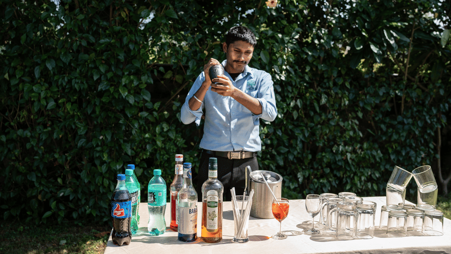 Corbett Nirvana Resort featuring a person stands behind an outdoor bar counter mixing a drink with bottles and glasses on the table.