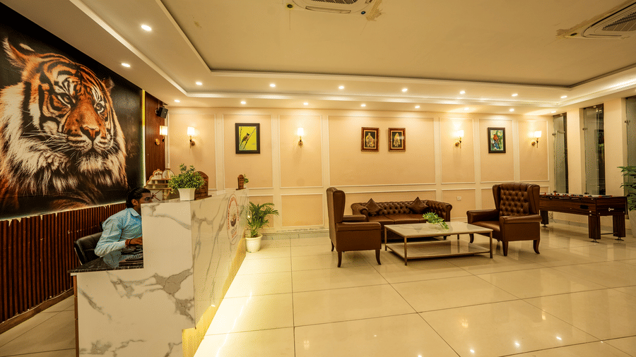 A reception desk at Corbett Nirvana Resort standing at the end of a lobby containing sofas and a coffee table.