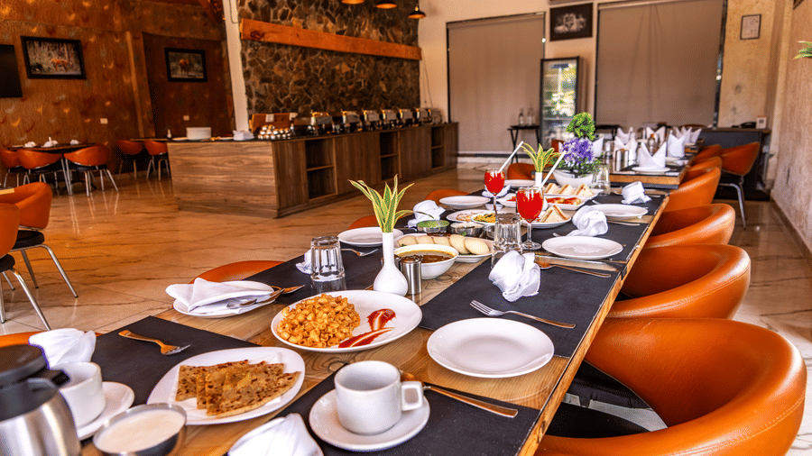 Corbett Nirvana Resort featuring a long rectangular table is laid with plates, cutlery, and cups inside a restaurant.