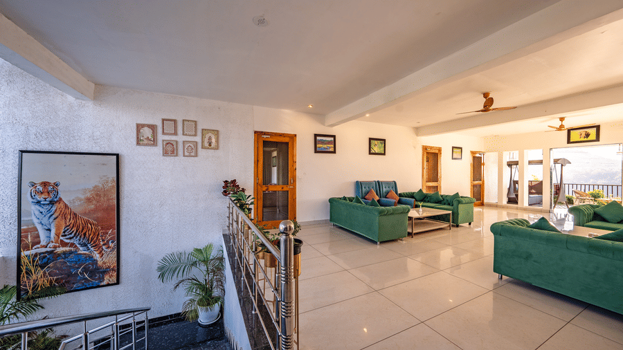 A lounge area at the Corbett Nirvana Resort featuring sofas sits at the top of a staircase next to a wall with pictures.
