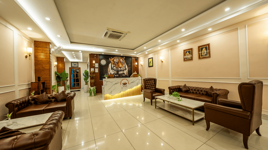 A person sitting behind a reception desk in a room with seating and a picture of a tiger on the wall  at the Corbett Nirvana Resort.