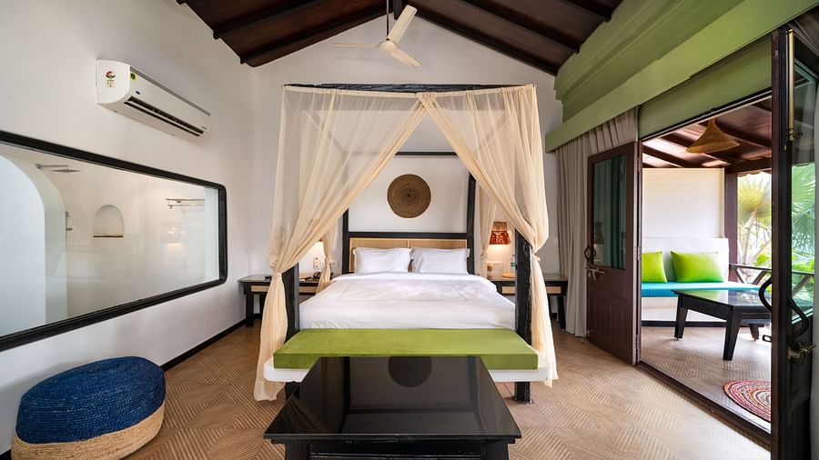 Elegant bedroom with a canopy bed, vibrant green accents, artistic wall decor, and a seating area opening to a private patio with outdoor seating