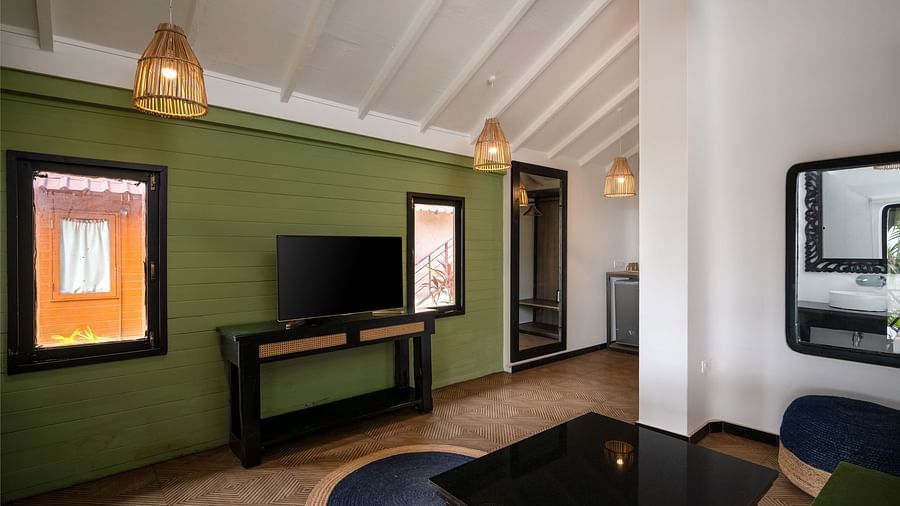 Modern living room with a green accent wall, a flat-screen TV on a wooden stand, elegant pendant lights, and cosy seating with natural light