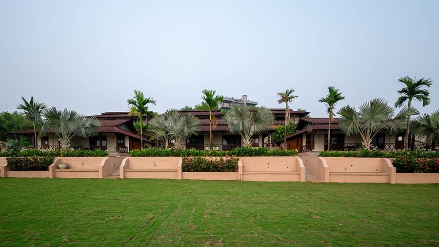 A lawn in front of the facade of a long building, surrounded by palm trees and other greenery - Crescent Resort, Goa.