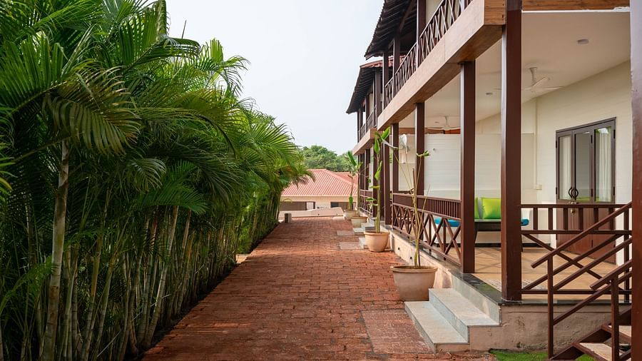 A clay-tiled pathway with a building on the right-hand side and small bamboo shoots lining the left-hand side - Crescent Resort, Goa.