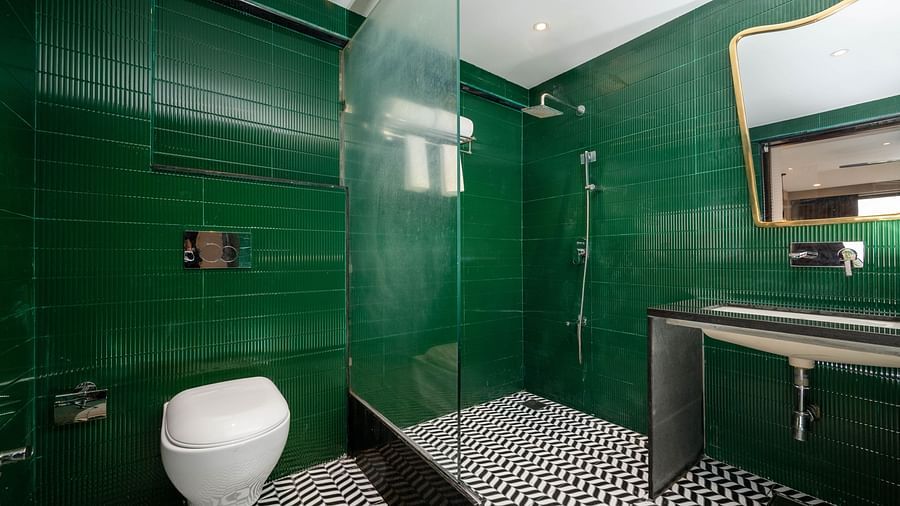 An image showing a commode, a glass partition, a wash basin with a large mirror upfront.