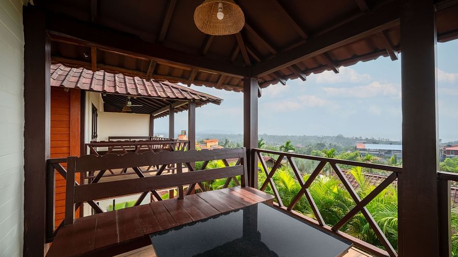 An image showing a balcony view with greenery, shot from a room with wooden details and benches