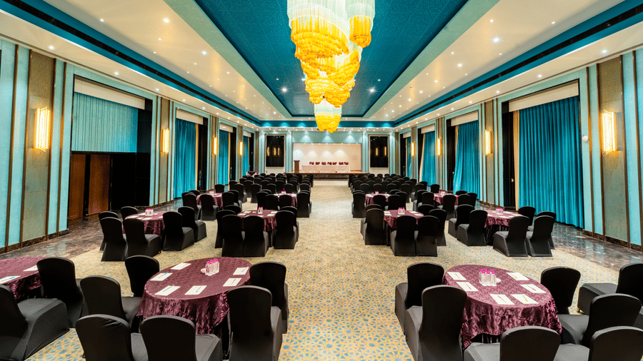 A banquet hall at Crescent Resort, Sehore, with chandeliers, a stage, chairs, and tables arranged for an event.