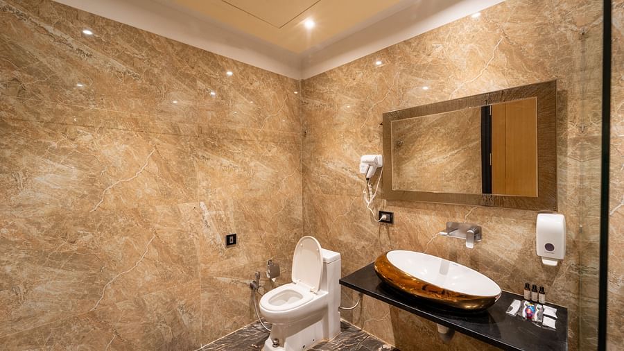 Club Room bathroom features a wall-mounted hand wash, hairdryer, a horizontally placed mirror above the wash basin, and a western toilet seat at Crescent Spa & Resort, Indore