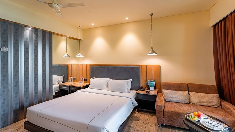 Club Room features bedside tables on both sides of the bed, a two-seater sofa with pillows, and a round table in front of it at Crescent Spa & Resort, Indore