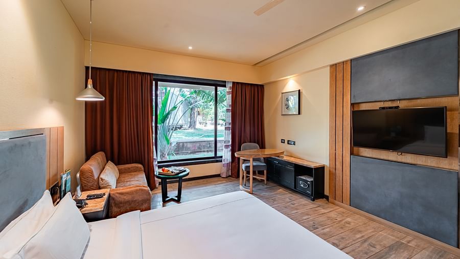 Club Room features a spacious bed, cushioned sofa, wall-mounted television, and a large window showcasing a natural view at Crescent Spa & Resort, Indore