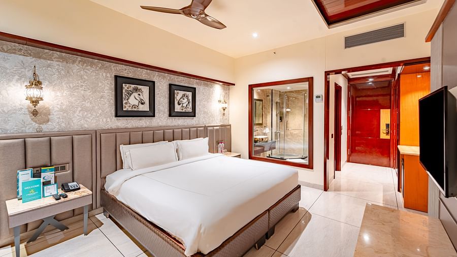 A spacious bed with two photo frames above, a bedside table with essentials, and a wall mounted TV opposite at  Crescent Spa & Resort, Indore