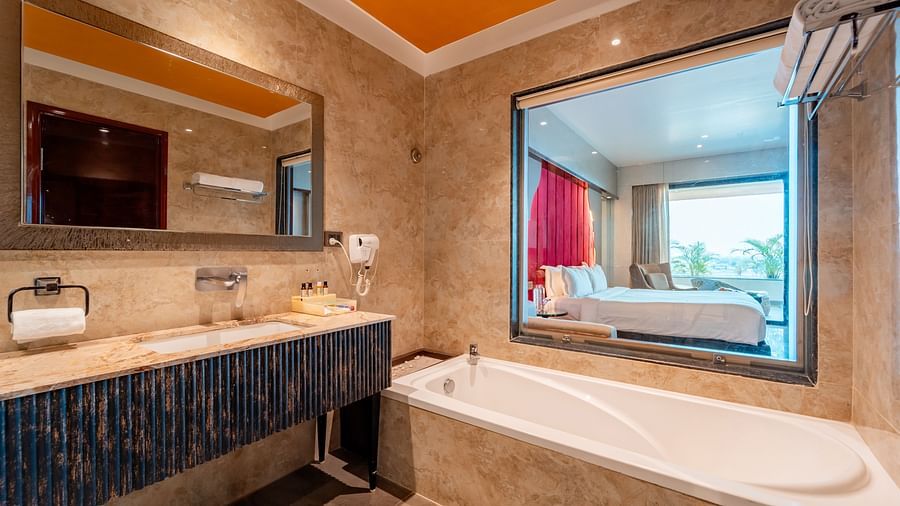 Executive Room bathroom features a bathtub to one side with a glass window showing the bedroom view, and an adjacent washbasin with a mirror above it at Crescent Spa & Resort, Indore
