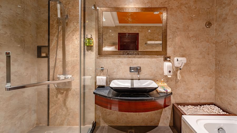 Executive Suite bathroom features a bathtub, a washbasin with a mirror above it, and a shower area separated by glass at Crescent Spa & Resort, Indore