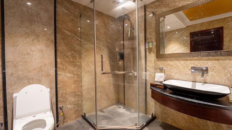 The Family Suite bathroom at Crescent Spa & Resort, Indore, includes a rectangular mirror above the washbasin, a glass panel separating the shower area, and a western toilet