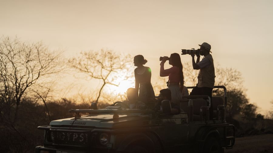 The silhouette of three people on a jeep clicking images with a camera -Daksh Eden Greenz, Sasan Gir.