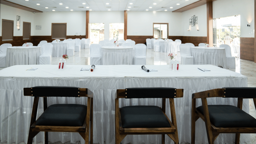 A neatly set-up banquet hall of Daksh Eden Greenz, furnished with chairs facing a table for the central panel.