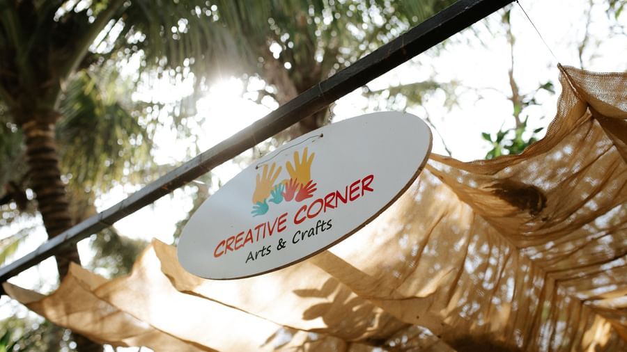 A sign board hung on a rod with the words 'creative corner' written on them and canopied by trees -Daksh Eden Greenz, Sasan Gir
