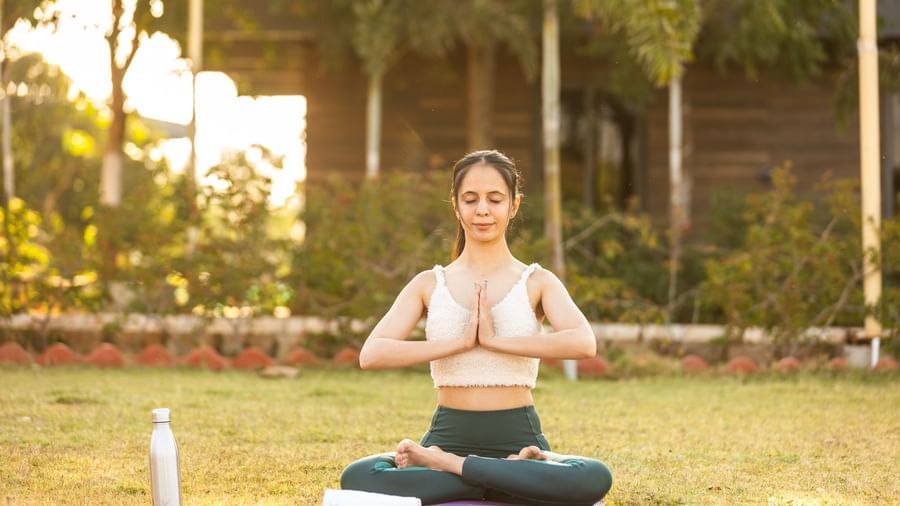 A woman in a praying pose practising yoga outdoors amidst greenery in Daksh Resort & Amusement Park.