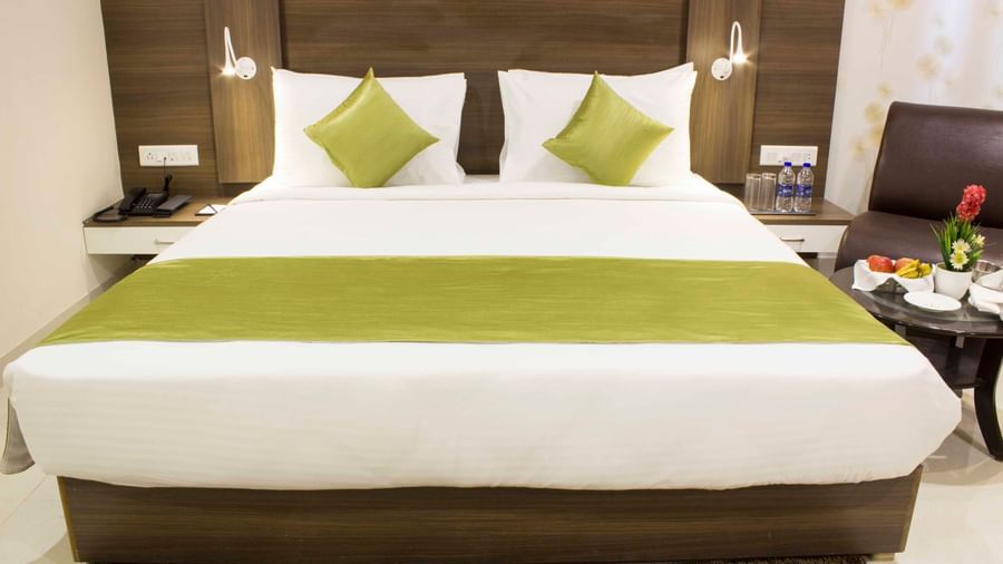 A hotel room with a clean bed, white sheets, and a decorative headboard | Daksh Comfort Room | Daksh The Madhuvan Suites