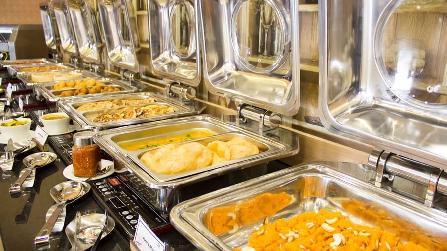 A close-up of a buffet with various dishes in chafing dishes | Daksh The Madhuvan Suites