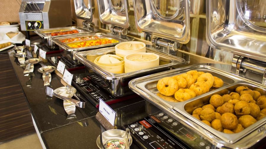 A close-up of a buffet with various dishes in chafing dishes | Daksh The Madhuvan Suites