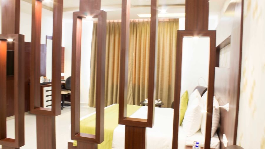A hotel room with a bed, flat-screen TV, and decorative wooden wall partitions | Daksh Suite | Daksh The Madhuvan Suites