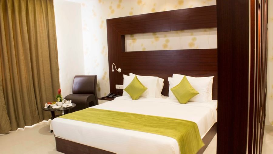 A hotel bedroom with a large bed, elegant wooden headboard, and green bed runner | Daksh Suite | Daksh The Madhuvan Suites