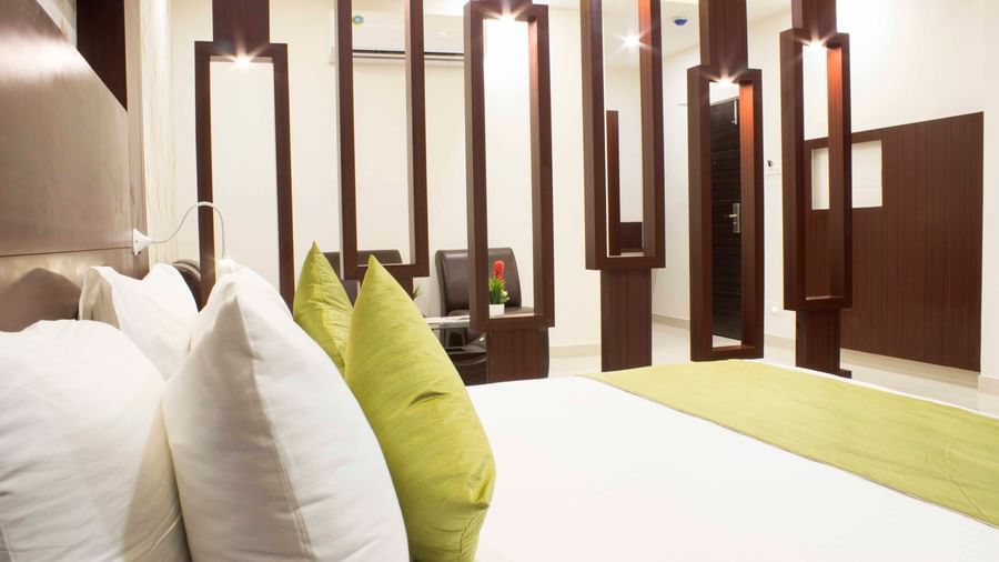 A close-up of a bed with white and green bedding and decorative pillows | Daksh Suite | Daksh The Madhuvan Suites