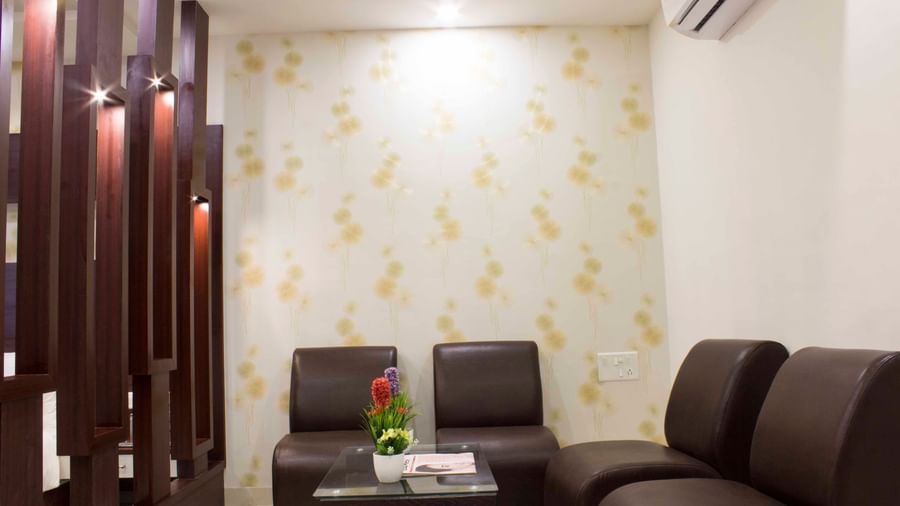A hotel living area with dark leather sofas, a glass table, and wooden room dividers | Daksh Suite | Daksh The Madhuvan Suites
