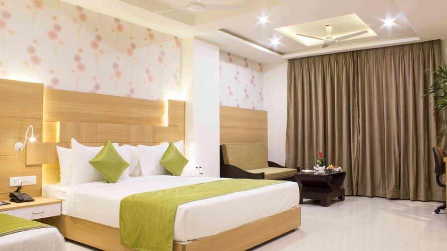 A hotel bedroom with a large bed, a single bed, light wood headboards, and green bed runners | Daksh Pride Room | Daksh The Madhuvan Suites