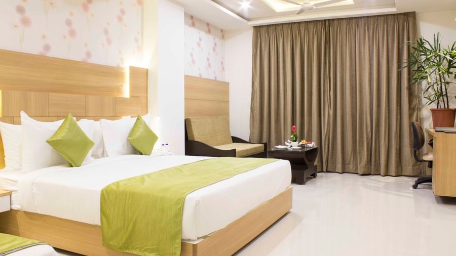 A hotel bedroom with a large bed, a single bed, light wood headboards, and green bed runners | Daksh Pride Room | Daksh The Madhuvan Suites