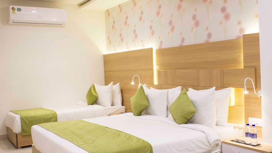 A hotel bedroom with a large bed, a single bed, light wood headboards, and green bed runners | Daksh Pride Room | Daksh The Madhuvan Suites