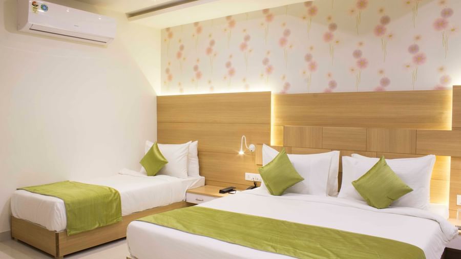A hotel bedroom with a large bed, a single bed, light wood headboards, and green bed runners | Daksh Pride Room | Daksh The Madhuvan Suites