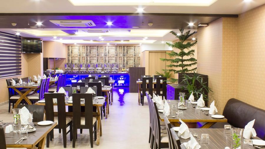 A hotel restaurant with set tables, dark chairs, and blue ambient lighting | Daksh The Madhuvan Suites