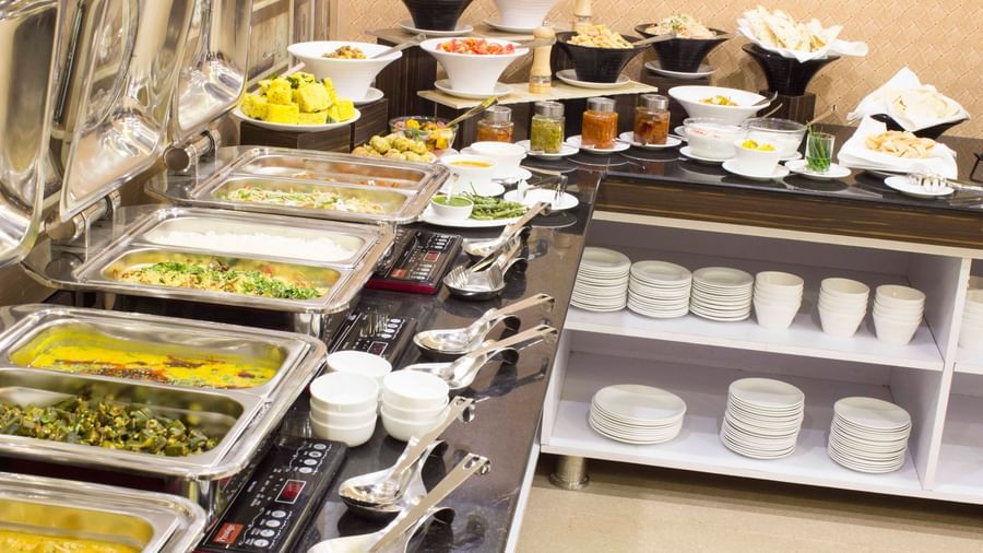A close-up of a buffet with various dishes in chafing dishes | Daksh The Madhuvan Suites