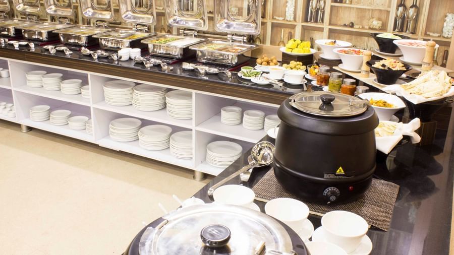 A close-up of a buffet with various dishes in chafing dishes | Daksh The Madhuvan Suites