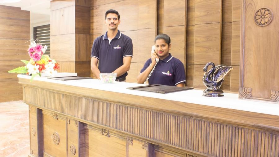 A hotel reception desk with two staff members smiling | Daksh The Madhuvan Suites