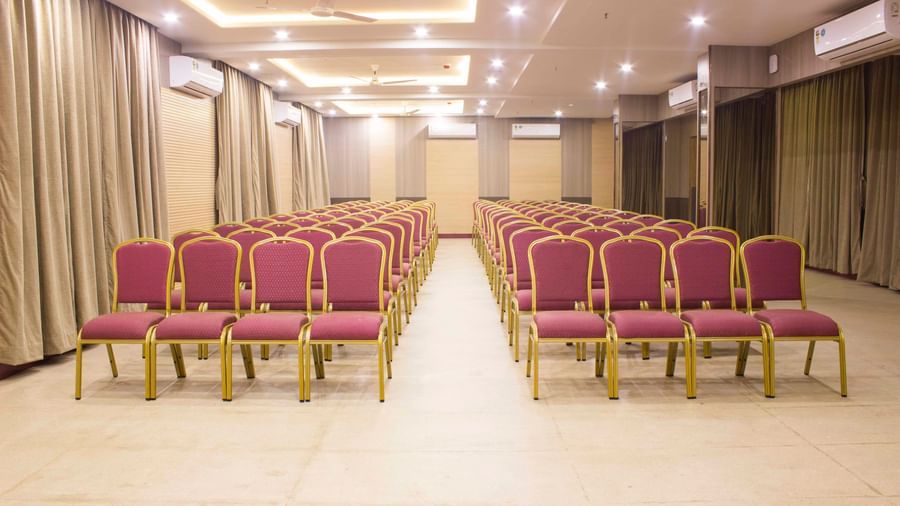 A wide shot of a banquet hall with multiple rows of empty pink and gold chairs. | Banquet Hall | Daksh The Madhuvan Suites