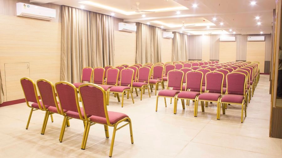 A wide shot of a banquet hall with multiple rows of empty pink and gold chairs. | Banquet Hall | Daksh The Madhuvan Suites