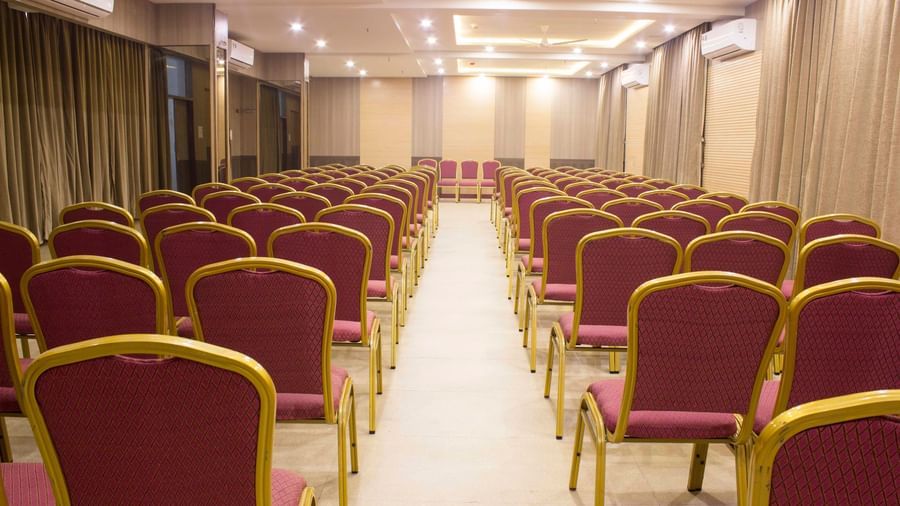 A wide shot of a banquet hall with multiple rows of empty pink and gold chairs. | Banquet Hall | Daksh The Madhuvan Suites