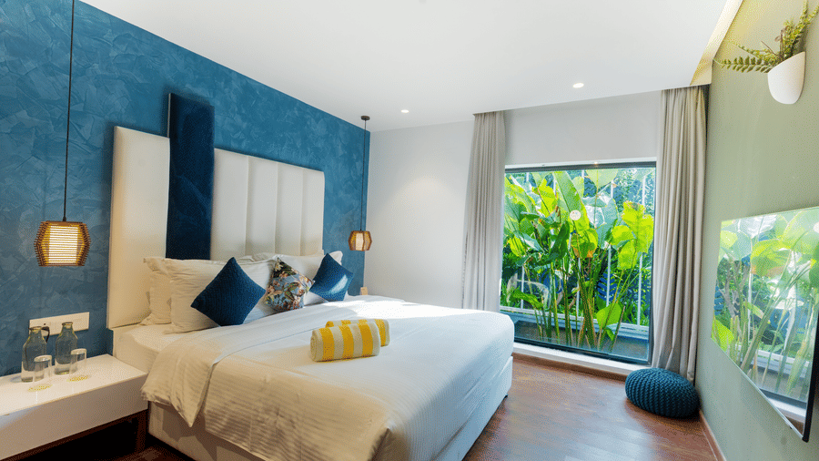 The bedroom of 2 Bedroom Villa at Darza Resorts featuring a large bed, patterned wall, and a full-length window overlooking lush tropical foliage