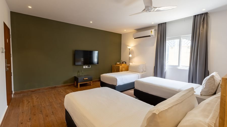 image of a bedroom with three single beds facing towards the tv wall mounted on an olive green coloured wall at the luxury group stay villa - Darza Resorts