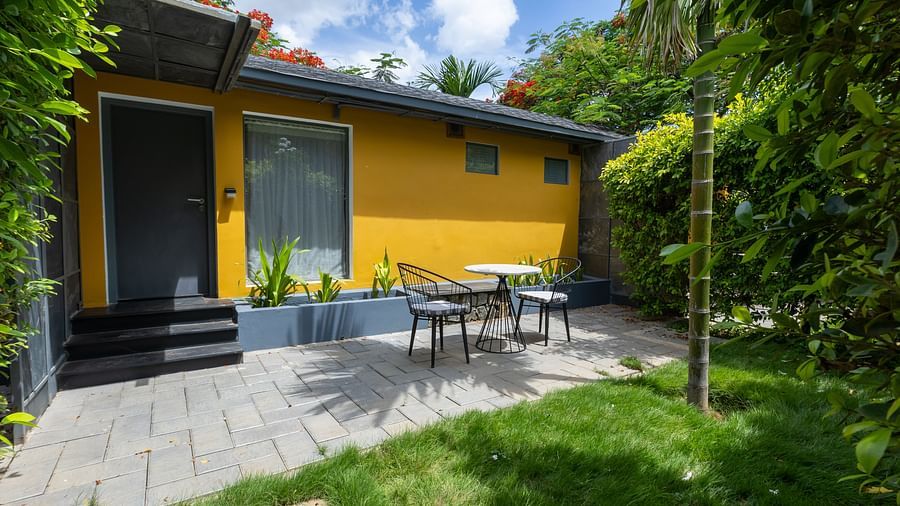 facade image of a villa with a yellow coloured exterior with a sit out area nestled amidst in lush greenery