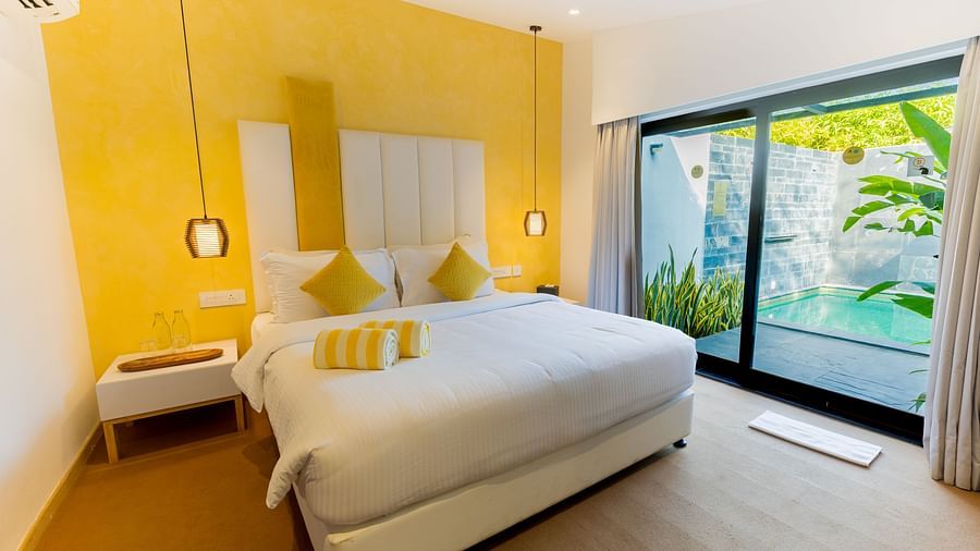 Pool Villa With Private Garden at Darza Resorts features a white bed with yellow cushions, a yellow accent wall, and a large sliding door revealing a private plunge pool