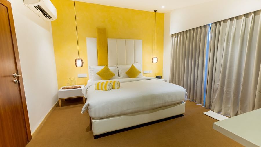 Pool Villa at Darza Resorts with a white bed, a bright yellow accent wall, and long grey curtains beside a large window. 