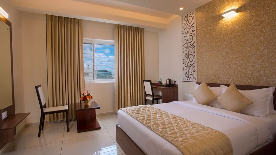 A hotel room with a comfortable bed, a wooden side table with flowers and a city view through the window - De Venetian by TGI, Brookefield